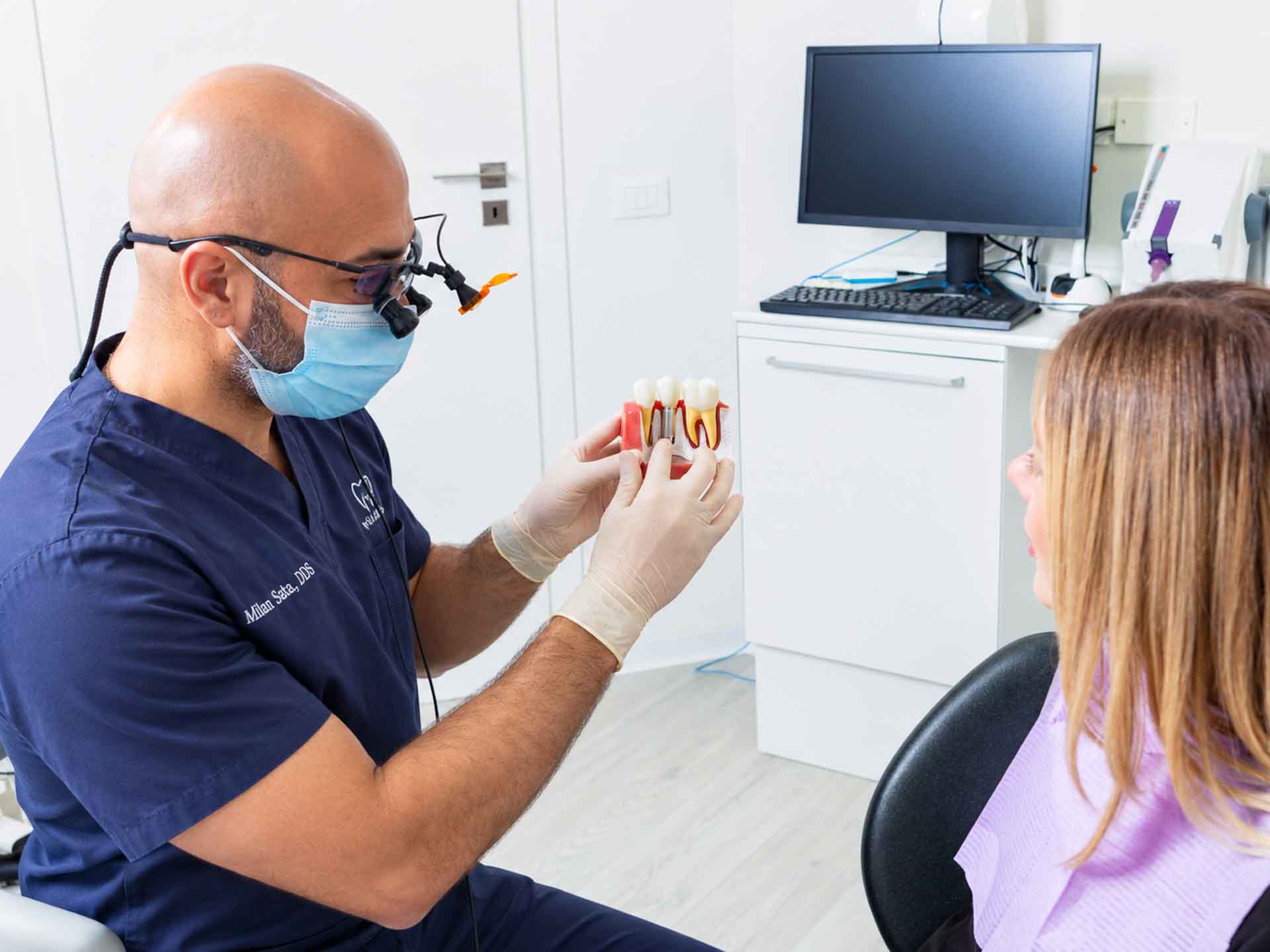 Dentist explaining a dental implant model to a patient during a consultation in Grand Blanc, Michigan